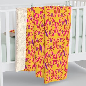 May include: A yellow fleece throw blanket with a pink and purple geometric pattern. The blanket has a soft, plush texture and is perfect for snuggling up on the sofa.