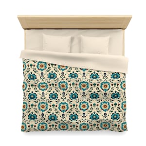 May include: A bed with a light wood headboard and two white pillows. The bed is covered with a duvet featuring a repeating floral pattern in teal, yellow, and red on a cream background. The duvet cover has a cream-colored underside.