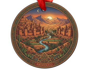 Op de afbeelding: Ronde ornament met een landschapsillustratie van Marokko. Het ontwerp toont een rivier, gebouwen, bergen en een zonsondergang. Het woord "MOROCCO" staat onderaan. Een rood lint is bevestigd om op te hangen.