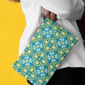 May include: A teal and yellow patterned clutch bag with a geometric design. The bag has a zipper closure and a black strap.