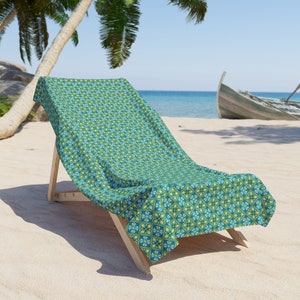 May include: A green and blue patterned beach chair with a wooden frame. The chair is on a sandy beach with palm trees and a wooden boat in the background.