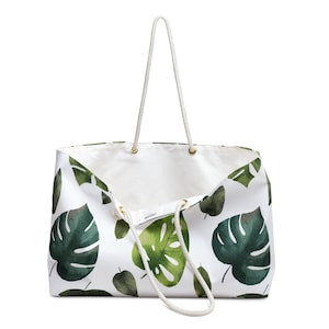 May include: White canvas tote bag with green tropical leaf print. The bag has two rope handles and a drawstring closure.