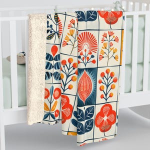 May include: A soft, plush throw blanket with a colourful floral pattern. The design features a variety of stylised flowers and leaves in shades of red, orange, yellow, blue, and white on a cream background.