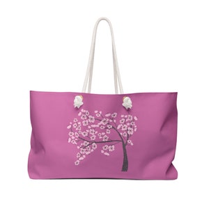 May include: A pink canvas tote bag with white rope handles and a black and pink floral design. The floral design is a stylized tree with pink flowers.