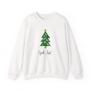 Può includere: Felpa bianca con un design di albero di Natale verde, una stella e dettagli floreali. Il testo "God Jul" è scritto in blu scuro. Un capo festivo per le festività natalizie.