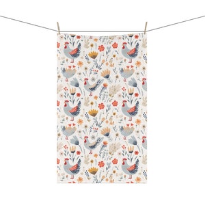 May include: A white towel with a repeating pattern of stylized chickens and flowers. The chickens are light blue with red accents, and the flowers are in shades of yellow, orange, and red. The towel is hanging from a clothesline.
