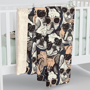 May include: A soft, plush fleece blanket with a repeating pattern of French Bulldogs wearing sunglasses. The dogs are illustrated in shades of black, white, and brown against a dark blue background.
