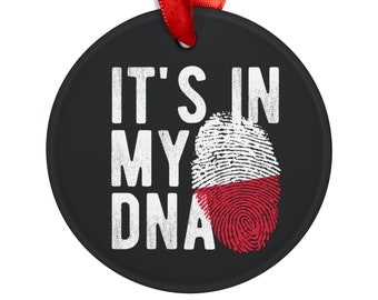 Może przedstawiać: Czarna, okrągła ozdoba z białym napisem "IT'S IN MY DNA". Wzór odcisku palca w barwach polskiej flagi: biało-czerwony. Czerwona wstążka do zawieszenia.