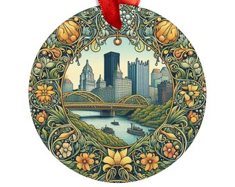 May include: A round, metal ornament featuring a detailed illustration of the Pittsburgh skyline with a bridge and river. The skyline is surrounded by a decorative floral border in shades of green, yellow, and brown.