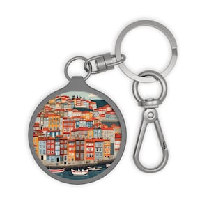 May include: A silver keychain with a round charm featuring a colorful illustration of a cityscape with buildings and a waterfront. The charm is attached to a silver split ring and a silver lobster clasp.