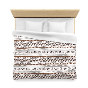 Op de afbeelding: Een witte dekbedovertrek met een bruin en wit patroon. Het patroon heeft herhalende swirls en stippen.