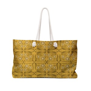 May include: A yellow tote bag with a white rope handle and a floral pattern. The pattern features brown leaves and white flowers.