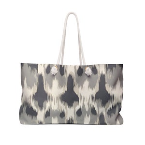 May include: A large, white canvas tote bag with a gray and white ikat pattern. The bag has white rope handles and gold metal accents.