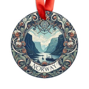 Puede incluir: Adorno redondo de metal con una ilustración detallada de un fiordo en Noruega. El adorno presenta un paisaje azul y verde con un barco navegando por el agua. El texto "NORWAY" está escrito en una fuente decorativa en la parte inferior del adorno.
