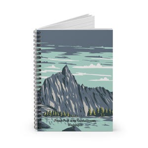 May include: Spiral-bound notebook featuring a landscape illustration of Prusik Peak in the Enchantments, Washington. The artwork depicts a mountain range, trees, and a lake in shades of gray, blue, and green. The text "Prusik Peak in the Enchantments Washington" is printed at the bottom.