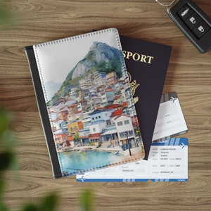 May include: A passport holder with a watercolor illustration of a colorful cityscape on a mountainside. The holder has a black border and a white background.