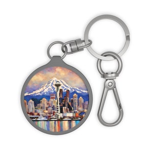 May include: A silver keychain with a round, metal charm featuring a colorful painting of the Seattle skyline with the Space Needle and Mount Rainier in the background.