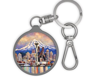 Puede incluir: Un llavero plateado con un dije redondo de metal que presenta una pintura colorida del horizonte de Seattle con la Space Needle y el Monte Rainier en el fondo.
