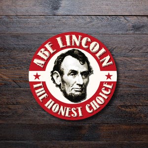Puede incluir: Un diseño gráfico circular rojo y blanco con el retrato de Abraham Lincoln y el texto "ABE LINCOLN" y "THE HONEST CHOICE". Dos estrellas rojas enmarcan el retrato. La imagen está sobre un fondo de madera oscura.