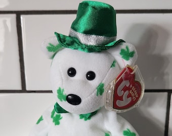 Peut inclure: Un ours en peluche blanc avec des trèfles verts, portant un chapeau et un nœud papillon verts. L'ours a des yeux et un nez noirs, et une étiquette rouge avec l'inscription "Beanie Babies". Un objet de collection sur le thème de la Saint-Patrick.