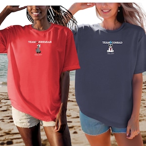 May include: Two short-sleeved t-shirts, one red and one navy blue. The red shirt has the text "TEAM JEREMIAH" and a graphic of a bear. The navy blue shirt has the text "TEAM CONRAD" and a graphic of a bear. Both shirts have the text "Class 2029".