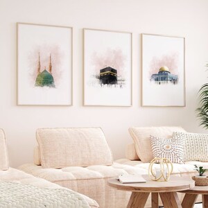 May include: Three watercolor prints of Islamic architecture. The prints are framed in gold and have a pink watercolor background. The prints are hung on a white wall.