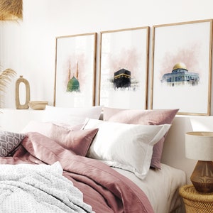 May include: Three framed watercolor paintings of Islamic architecture. The paintings are in a bedroom setting above a bed with pink bedding and a white blanket.
