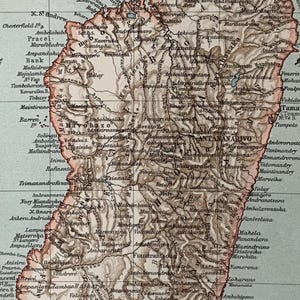 May include: A vintage map of Madagascar, depicting the island's geography and key cities. The map is printed in brown and black ink on a light blue background. The map includes the names of cities, rivers, and mountains.