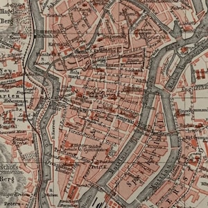 Può includere: Mappa antica di una città, con intricati tracciati stradali, corsi d'acqua e punti di riferimento etichettati. La mappa utilizza una combinazione di colori rosso e nero, con testo in tedesco. Documento storico.
