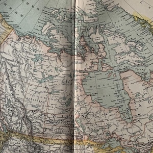 May include: A vintage map of North America showing the borders of the United States and Canada in detail. The map is printed in shades of blue, green, brown, and yellow. The map includes the text "HUDSON BAY" and "CANADA".