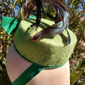 Peut inclure: Un chapeau en feutre vert avec une plume noire et un ruban vert.