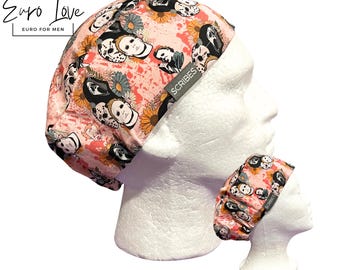 May include: A scrub cap featuring a pink background with a repeating pattern of horror movie characters and orange sunflowers. The fabric has a grey tag with the text SCRIBES printed in white. The cap is displayed on a white mannequin head.