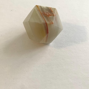May include: A faceted, geometric crystal with a pale, translucent appearance. The crystal features bands of orange and yellow hues running through its interior, creating a striking visual contrast. The crystal is set against a plain white background.