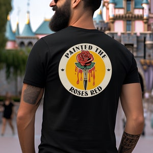 May include: Black t-shirt with a yellow circle graphic featuring a red rose with a dripping paintbrush and the text "Painted the Roses Red".