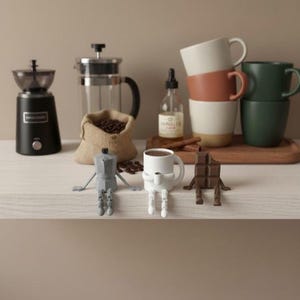 May include: A still life arrangement featuring coffee-related items. Includes a black coffee grinder, a French press, a burlap sack of coffee beans, and a bottle of vanilla extract. There are also several stacked mugs and whimsical coffee-themed figurines.