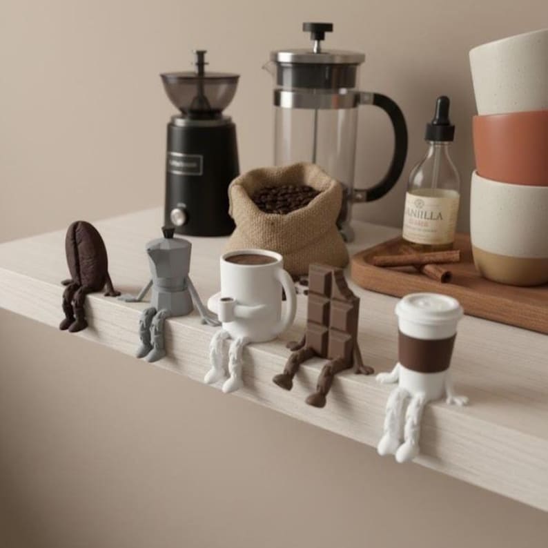 May include: A collection of whimsical coffee-themed figurines, including a coffee bean, a stovetop espresso maker, a coffee cup, a chocolate bar, and a to-go coffee cup, each with legs. A coffee grinder, French press, and coffee beans in a burlap sack are in the background.