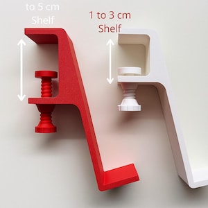 May include: Two clamp-style shelves, one red and one white, are displayed against a neutral background. The red shelf is designed for shelves up to 5 cm, while the white shelf accommodates shelves from 1 to 3 cm. Text indicates shelf size.