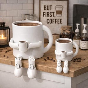 May include: Two white ceramic coffee mugs with arms and legs, each holding a smaller mug. The mugs are filled with coffee. A sign in the background reads "BUT FIRST, COFFEE". Coffee beans are scattered on the wooden surface.
