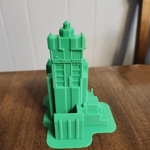 Puede incluir: Un modelo verde impreso en 3D del Hollywood Tower Hotel de los estudios Hollywood de Disney. El modelo está detallado con el texto icónico "Hollywood Tower" en la parte delantera.