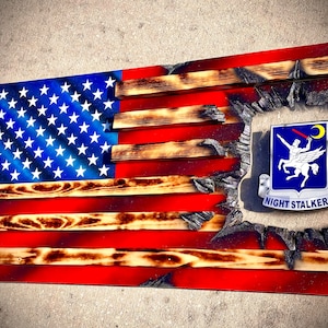 May include: A wooden American flag with a distressed, burnt look. The flag is broken in the center, revealing a blue and white patch with a winged horse and the text "NIGHT STALKERS".