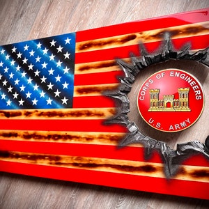 May include: A wooden American flag with a distressed look, featuring a black and gray circular design with the words "Corps of Engineers U.S. Army" in gold lettering.