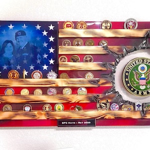 May include: A wooden American flag shadow box display with a photo of a couple in the center. The shadow box has shelves for displaying military challenge coins and medals. The text "SFC Hays - Ret 2020" is at the bottom of the display. The shadow box has a distressed wood finish and a red, white, and blue color scheme.