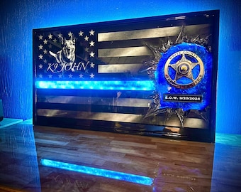 Op de afbeelding: Een ingelijste Amerikaanse vlag met een blauwe lijn, een politiebadge en de tekst "K9 JOHN" en "E.O.W. 9/20/2024".