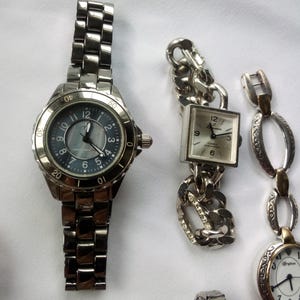 May include: A collection of eight wristwatches with silver, gold, and turquoise accents. The watches have different styles of bands, including chain link, oval link, and a traditional metal band.