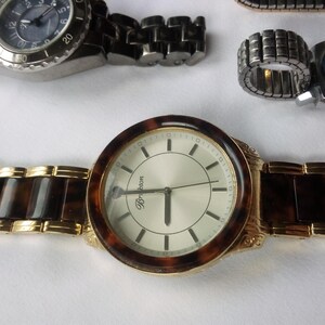 May include: A gold-tone wristwatch with a white face and black hands. The watch has a brown tortoiseshell band and the word "Brighton" is printed on the face.