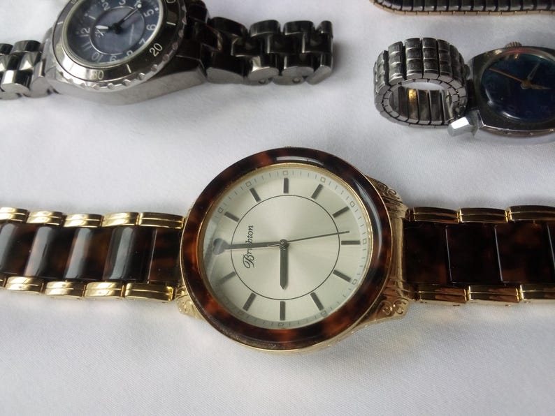 May include: A gold-tone wristwatch with a white face and black hands. The watch has a brown tortoiseshell band and the word "Brighton" is printed on the face.