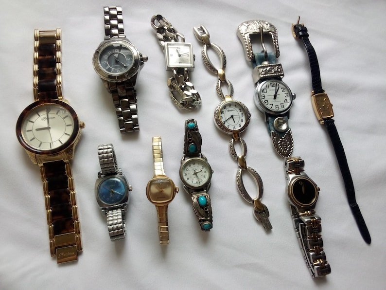 May include: A collection of ten wristwatches with various styles and designs. The watches feature different colored bands, including brown, black, silver, and gold. Some watches have round faces, while others have square or rectangular faces.