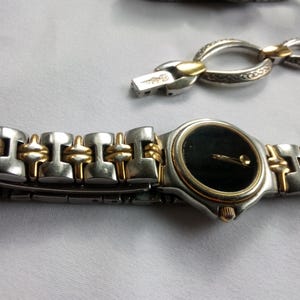 May include: A silver and gold tone wristwatch with a black face and a two-tone metal band.
