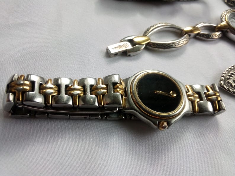 May include: A silver and gold tone wristwatch with a black face and a two-tone metal band.