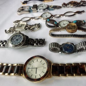 May include: A collection of ten wristwatches with various styles of bands and faces. The watches have silver, gold, and brown bands. Some of the watches have round faces, while others have square faces.